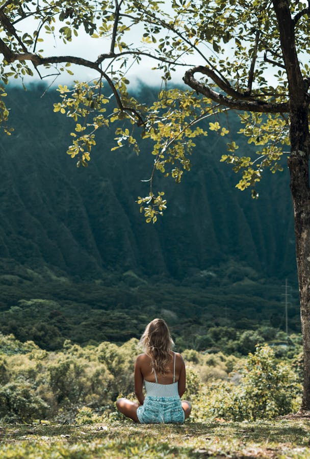 Unrecognizable female meditating on grass in highlands on sunny day