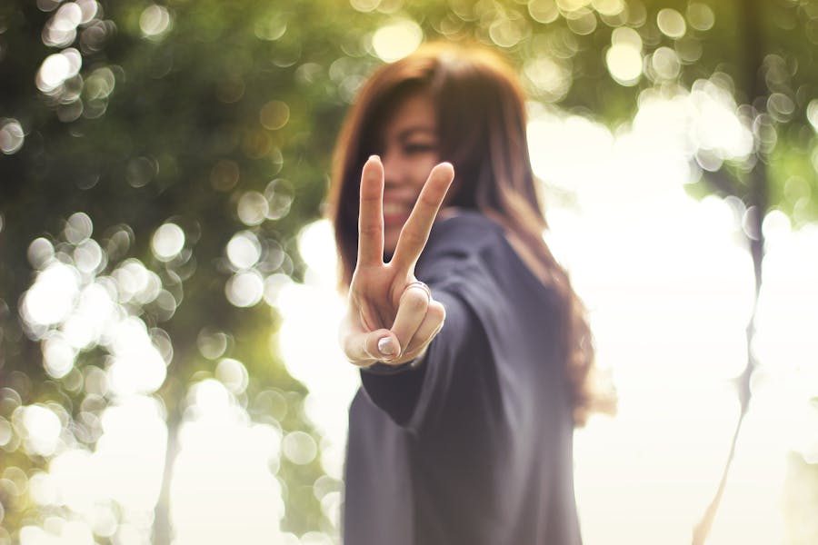 A joyful woman showing a peace sign with a blurred nature background.