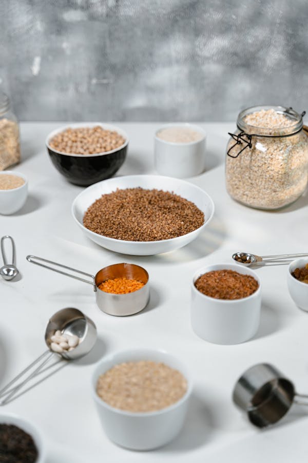 Assorted grains and pulses arranged on a white surface with bowls and measuring cups.