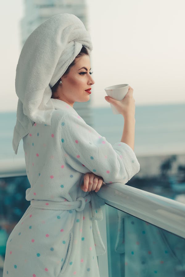 Woman in a bathrobe enjoying a morning coffee on a balcony with ocean view, embodying relaxation and leisure.