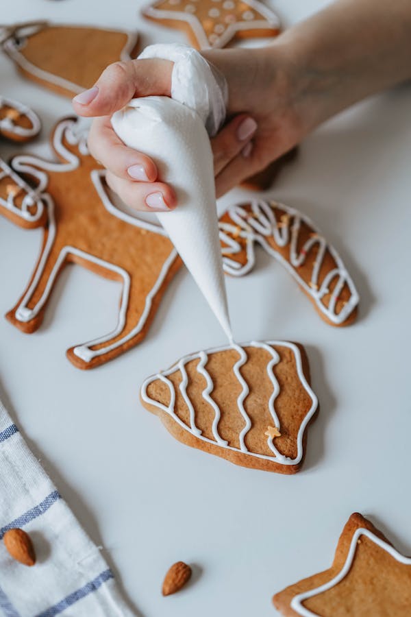 A close-up of a hand decorating festive gingerbread cookies with white icing.