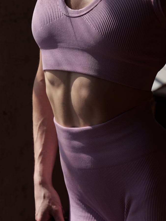 Close-up of a fit woman's abdominal area in athletic wear, emphasizing her toned muscles.